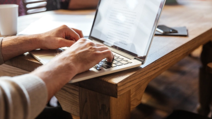 Zoom sur les mains d'un homme qui pianote sur son ordinateur portable.